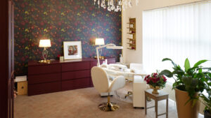 Beratungsbereich mit floraler Akzentwand, weißem Kosmetikstuhl, dekorativer Beleuchtung und grünen Zimmerpflanzen.