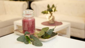 Dekoratives Glas mit rosafarbener Kerze und Eukalyptuszweigen auf einem Tisch in einem hellen, gemütlichen Wartebereich.